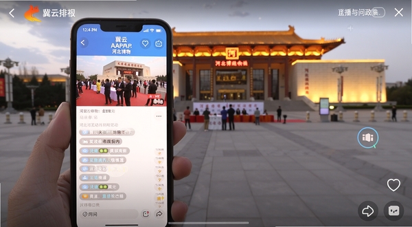 冀云APP直播互动与问政界面截图,画面中手机屏幕显示直播画面与网友评论滚动区,背景为河北博物院广场,暖色调灯光,画面富有现场感和互动氛围