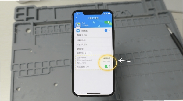 上海公交查询APP在手机设置中开启自启动权限的操作示意图,画面主体为手机屏幕显示应用管理界面与权限开关高亮标注,背景为简洁的灰色工作台,风格为步骤说明图